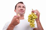 handsome man eating a green grapes, isolated on white background. Studio shot.