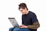 Happy male teenager sitting at computer and surfing in the internet