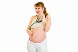 Happy pregnant woman with stethascope showing thumbs up gesture
