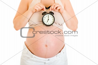 Pregnant woman holding alarm clock near her tummy.  Close-up.
