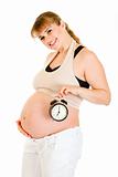 Smiling pregnant woman holding alarm clock near her belly
