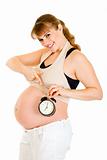 Smiling pregnant woman pointing on alarm clock
