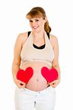 Smiling pregnant woman holding paper hearts near her belly

