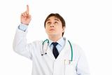 Serious young medical doctor pointing finger up

