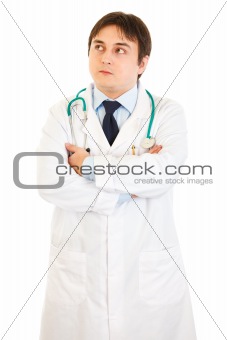Thoughtful doctor with crossed arms on chest looking up at copy space
