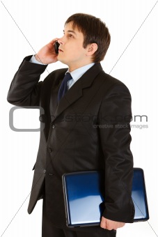 Serious modern businessman holding laptop and talking on mobile
