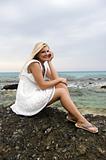 Young beautiful fresh woman sitting on a stone near the sea