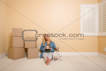 Pretty Woman Sitting on Floor with Cup Next to Moving Boxes and Dog in Empty Room.