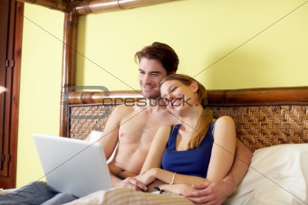 young couple lying on bed with pc