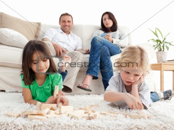 Proud parents looking at their children playing with dominoes on