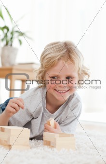 Cute little boy playing with dominoes lying on the floor