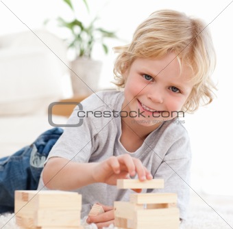 Happy boy playing with dominoes lying on the floor