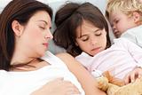 Adorable brother and sister sleeping with their mother in her be