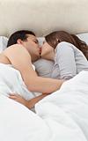 Adorable couple kissing while relaxing on the bed 