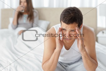 Man having a headache sitting on the bed with his girlfriend