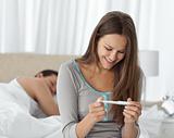 Happy woman looking a pregnancy test while her boyfriend sleepin