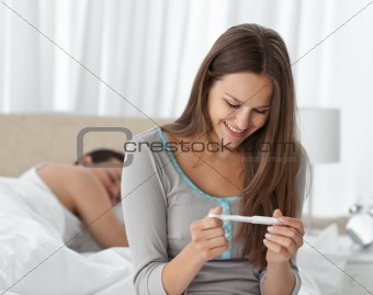 Happy woman looking a pregnancy test while her boyfriend sleepin