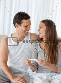 Happy couple with a pregnancy test sitting on the bed