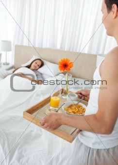 Lovely man bringing the breakfast to his girlfriend lying on the