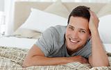 Joyful man lying on th edge of his bed at home