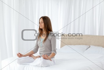 Pretty woman doing yoga exercises sitting on her bed