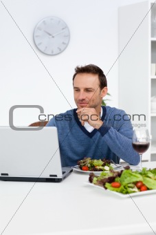 Handsome man looking at his laptop while having lunch