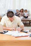 Man calculating his bills while his family are on the sofa