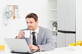 Businessman drinking while he is looking at his laptop