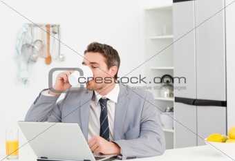 Businessman drinking while he is looking at his laptop