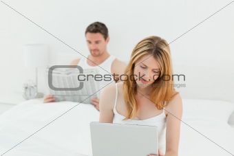 Woman is on her laptop while her husband is reading newspaper 