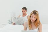Woman is on her laptop while her husband is reading newspaper 