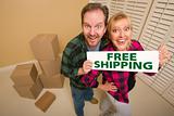 Goofy Couple Holding Free Shipping Sign in Room with Packed Cardboard Boxes.