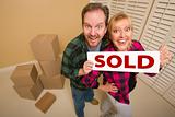Goofy Couple Holding Sold Sign in Room Surrounded by Cardboard Boxes.