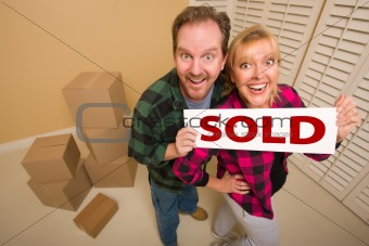 Goofy Couple Holding Sold Sign in Room Surrounded by Cardboard Boxes.