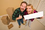 Goofy Thumbs Up Couple Holding Blank Sign in Room with Packed Cardboard Boxes.
