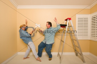Fun Couple Playing Sword Fight with Paint Rollers in Room - Ladder and Paint Tray Near.