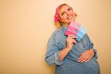 Smiling Pensive Pregnant Woman Leaning Against Wall Holding Pink and Blue Paint Swatches.
