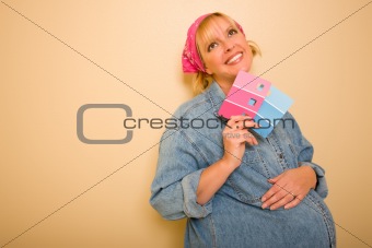 Smiling Pensive Pregnant Woman Leaning Against Wall Holding Pink and Blue Paint Swatches.
