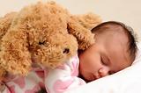 baby sleeps with brown toy dog on her back