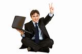Sitting on  floor with laptop smiling businessman showing victory gesture
