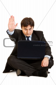 Sitting on  floor with laptop serious businessman showing stop gesture
