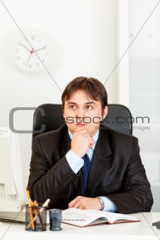 Pensive young businessman sitting at desk and planning timetable in diary
