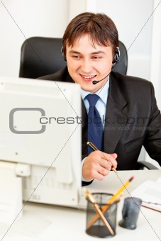 Smiling  businessman with  headset sitting at office desk and looking at computer monitor
