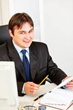 Smiling businessman sitting at office desk and working with documents
