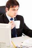 Thoughtful businessman  sitting at office desk  and holding cup of tea in hand
