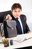 Attentive businessman sitting at office desk and giving briefcase
