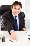 Smiling  businessman sitting at office desk and pointing on document for signature
