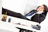 Happy  businessman sitting in office with feet on desk and talking on mobile phone
