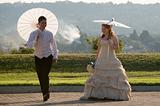 bride and groom walking outside in sun with umbrellas jumping