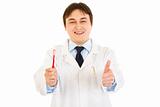 Smiling dentist holding toothbrush and showing  thumbs up gesture
